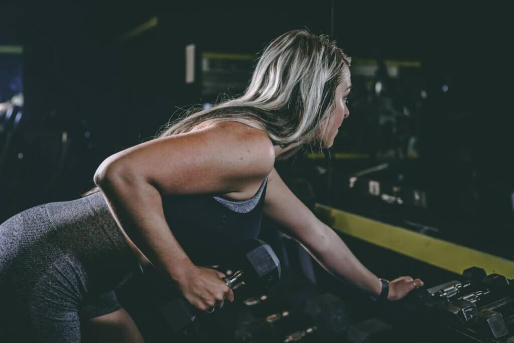 Side view of anonymous young sportswoman in active wear doing dumbbell row while exercising in gym and looking forward